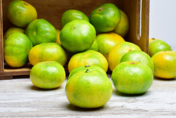 Close up, tangerine with green skin, more units behind in a group, next to a lying wooden box.