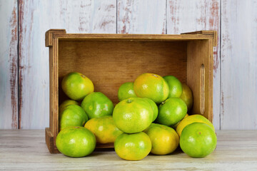 Tangerine with green skin, more units behind in a group, next to a lying wooden box. Copy space.