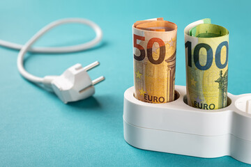 Fifty and one hundred euro banknotes plugged into a white power strip over blue bacground....