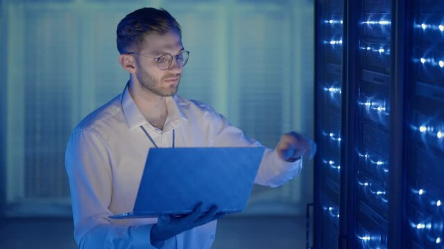 Male Server Engineer in Data Center. IT engineer inspecting a secure server cabinet using modern technology laptop coworking in data center.