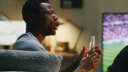 African American fan drinking beer and speaking with friend during match