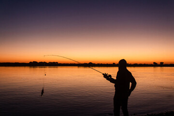 Silhouette of a young man catching a fish with the sunset in the background.