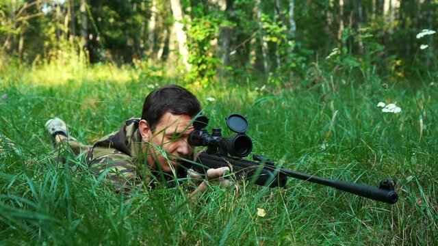 man aiming with a sniper rifle lying on the grass.