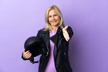 Middle age woman holding a motorcycle helmet isolated on purple background shaking hands for closing a good deal
