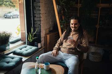 Young man hipster using his smartphone, sitting in a coffeehouse and drinking coffee.