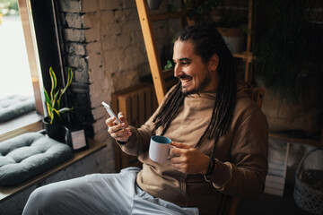 Young man hipster using his smartphone, sitting in a coffeehouse and drinking coffee.