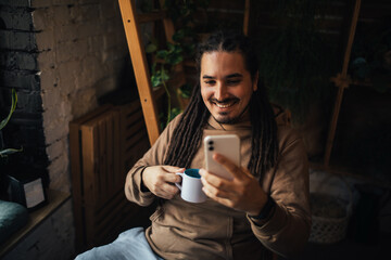 Young man hipster using his smartphone, sitting in a coffeehouse and drinking coffee.