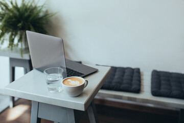 Cup with fresh coffee cappuccino and laptop on a white table.