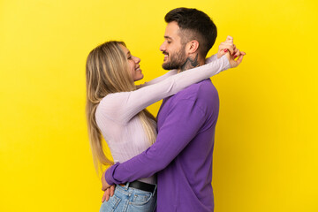 Young couple over isolated yellow background hugging