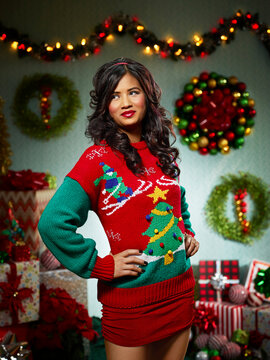 Portrait of woman in ugly Christmas sweater looking off camera against a Christmas themed backdrop.