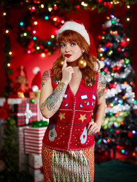Portrait of red headed woman with tattoos in ugly Christmas sweater/vest making a provocative face
