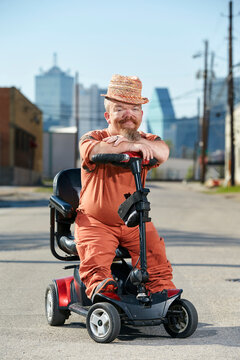 Portrait of male dwarf in sitting on scooter, looking into camera with big smile. 