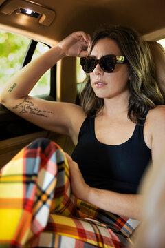 Portrait of casually dressed woman in sunglasses with tattoos sitting in backseat of luxury sedan 