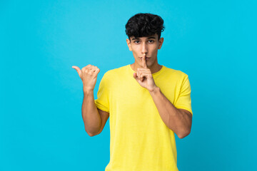 Young Argentinian man isolated on background pointing to the side and doing silence gesture
