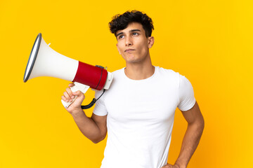 Young Argentinian man isolated on yellow background holding a megaphone and thinking