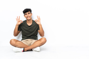 Young Argentinian man sitting on the floor showing an ok sign with fingers