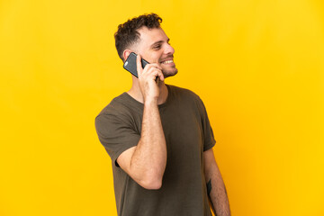 Young caucasian handsome man isolated on yellow background keeping a conversation with the mobile phone with someone