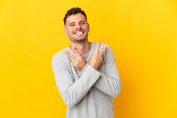 Young caucasian handsome man isolated on yellow background smiling and showing victory sign