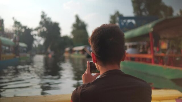 Young man recording the Xochimilco lake and Mexican trajineras with his phone