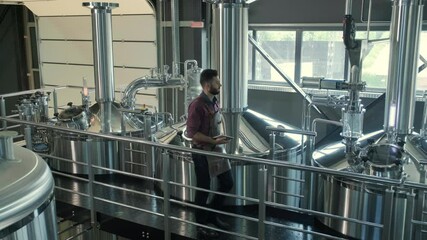 Young male brewer wearing a leather apron supervise the process of beer fermentation at a modern brewery factory - Powered by Adobe