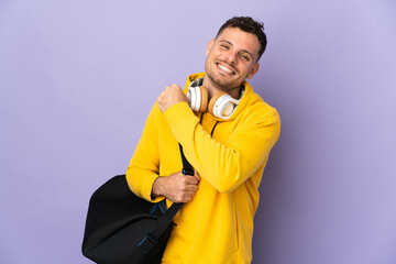 Young sport caucasian man with bag isolated purple background celebrating a victory