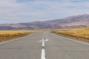 A road with markings along the valley against the background of a mountain range in autumn. Altai, Russia.