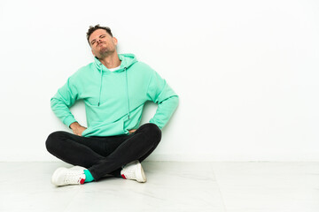 Young handsome caucasian man sitting on the floor suffering from backache for having made an effort