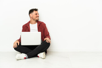 Young handsome caucasian man sit-in on the floor with laptop in lateral position