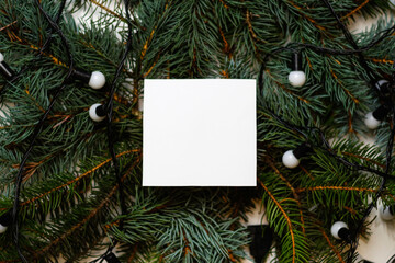 Defocus blank white card on natural christmas background with white lamps. Creative layout made of Christmas tree branches with paper card note. Decorative festive frame. Out of focus