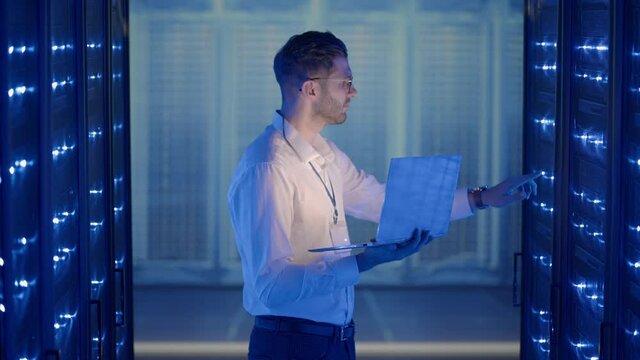 Male Server Engineer in Data Center. IT engineer inspecting a secure server cabinet using modern technology laptop coworking in data center.