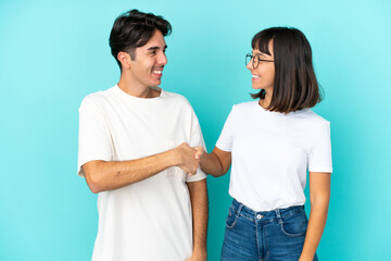 Young mixed race couple isolated on blue background handshaking after good deal