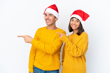 Young mixed race couple celebrating Christmas isolated on white background pointing finger to the side in lateral position