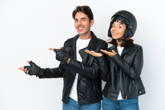 Young mixed race couple with a motorcycle helmet isolated on white background extending hands to the side for inviting to come