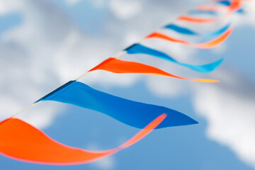 Small colorful orange and blue triangular flags against the sky background. Festival decor.