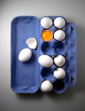 Aerial view of whole eggs and cracked egg showing yoke and broken shell in blue egg carton