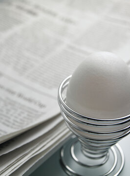 Boiled egg in wire egg cup on breakfast table with news paper