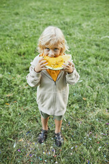 Vertical full length portrait of cute boy eating watermelon outdoors and smiling at camera