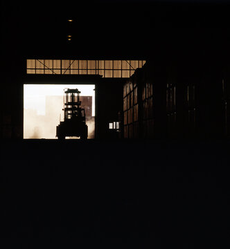Forklift leaving industrial warehouse entrance with shipping container