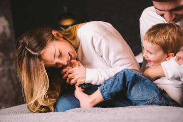 Parents with their baby boy on bed at home. Families with child in bed at night at home. Happy family enjoying in bed. Mom, dad and kid play in the bedroom in the evening. Loft style interior