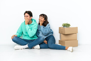 Young couple making a move while picking up a box full of things sitting on the floor isolated on white background shouting with mouth wide open to the lateral