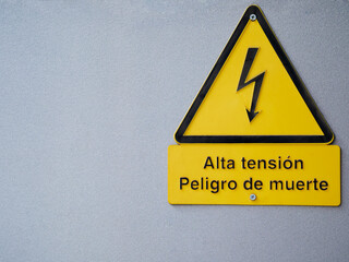 Yellow and black high voltage and danger of death sign prevents accidents. Text in spanish. Selective focus gray rough metal background. Copy space.