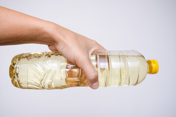 Hand holding a plastic bottle of sunflower oil for cooking against white background