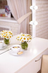 Client's place in hairdressing and beauty salon with cup of tea, macaroon and chamomiles in vase