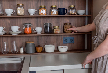 Organization of space the kitchen concept.Smooth shelves with glass jars. Woman hand reaches for jar with pasta