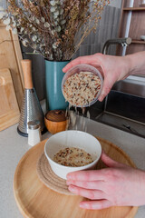 Senior woman pours cereals from plastic container into glass jar.