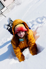 Fototapeta na wymiar Girl in a yellow jacket is lying in the snow. Sunny snowy day for fun.