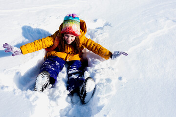 Fototapeta na wymiar Girl in a yellow jacket is lying in the snow. Sunny snowy day for fun.