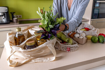 Adult woman pulls out the purchased products from farmers market from the fabric bags. Zero waste concept.