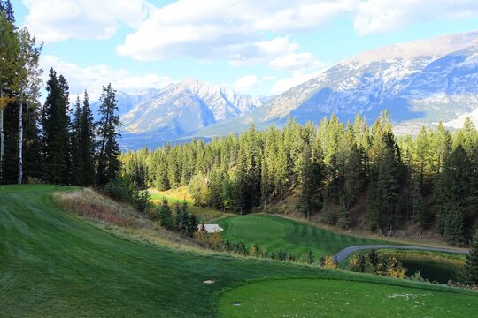 A beautiful view of a par 3 golf hole on a course with mountains in the background, surrounded by forest, on a beautiful sunny day with blue sky, in the rocky mountains near Banff, Alberta