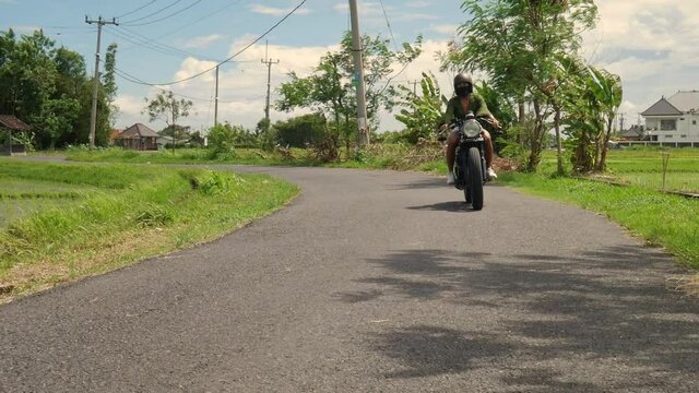 Asian Girl riding Suzuki Thunder 250cc Cafe Racer motorcycle wearing white hotpants and a olive green shirt. Pan shot on a street surrounded by fields. The bike approaching the camera.
